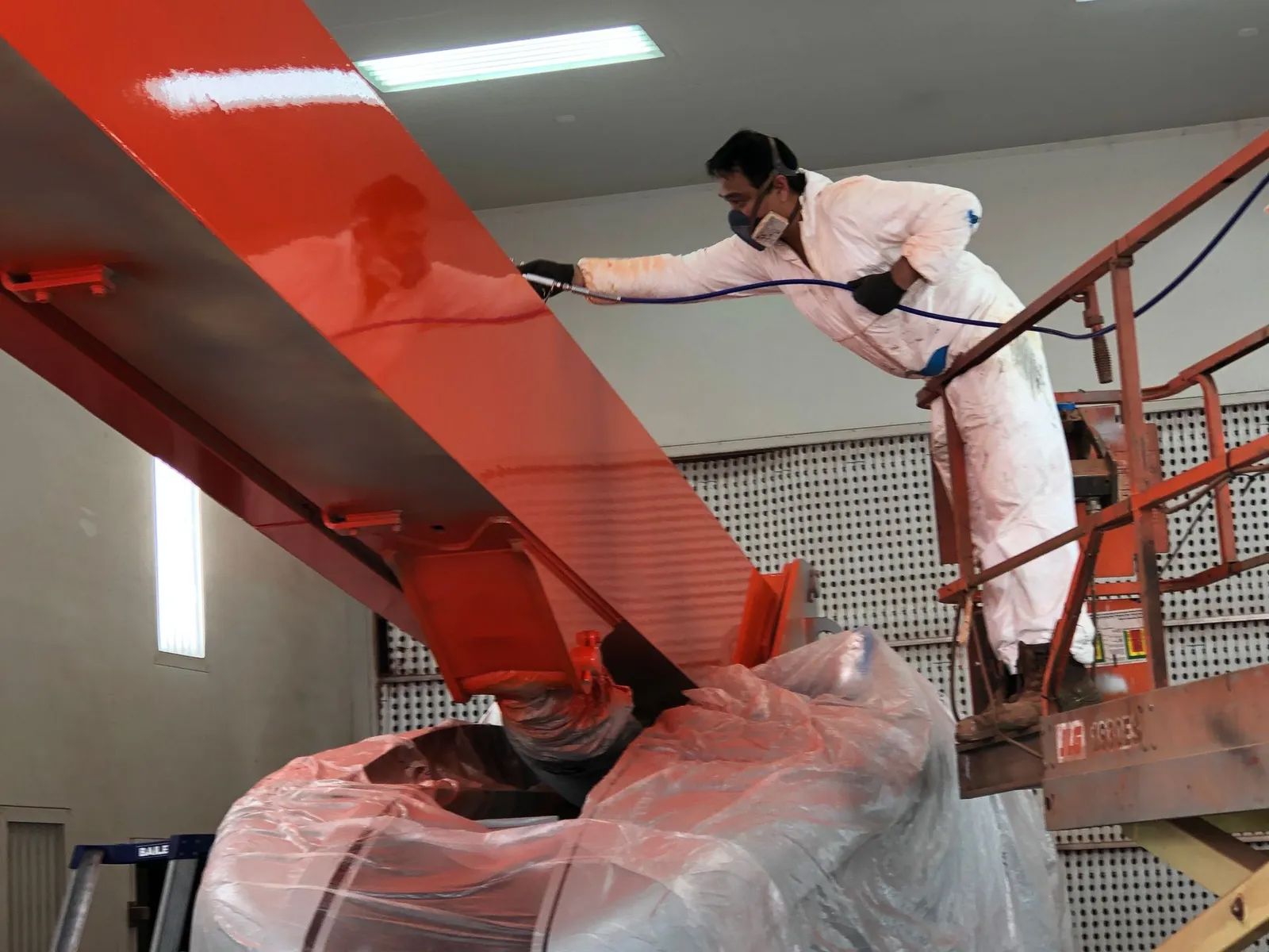 Worker Spray-painting a Large Red Structure Indoors — Paint Place Cowra in Orange, NSW