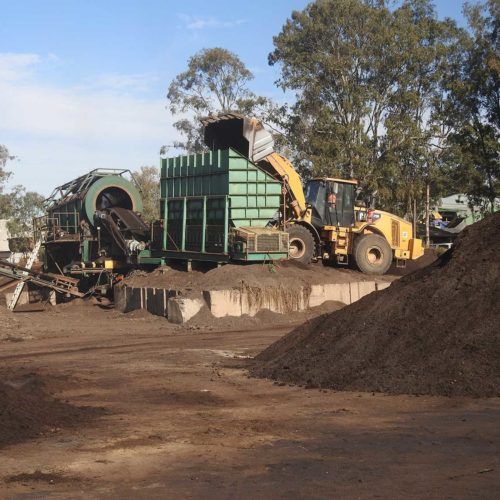 A bulldozer is loading dirt into a green container
