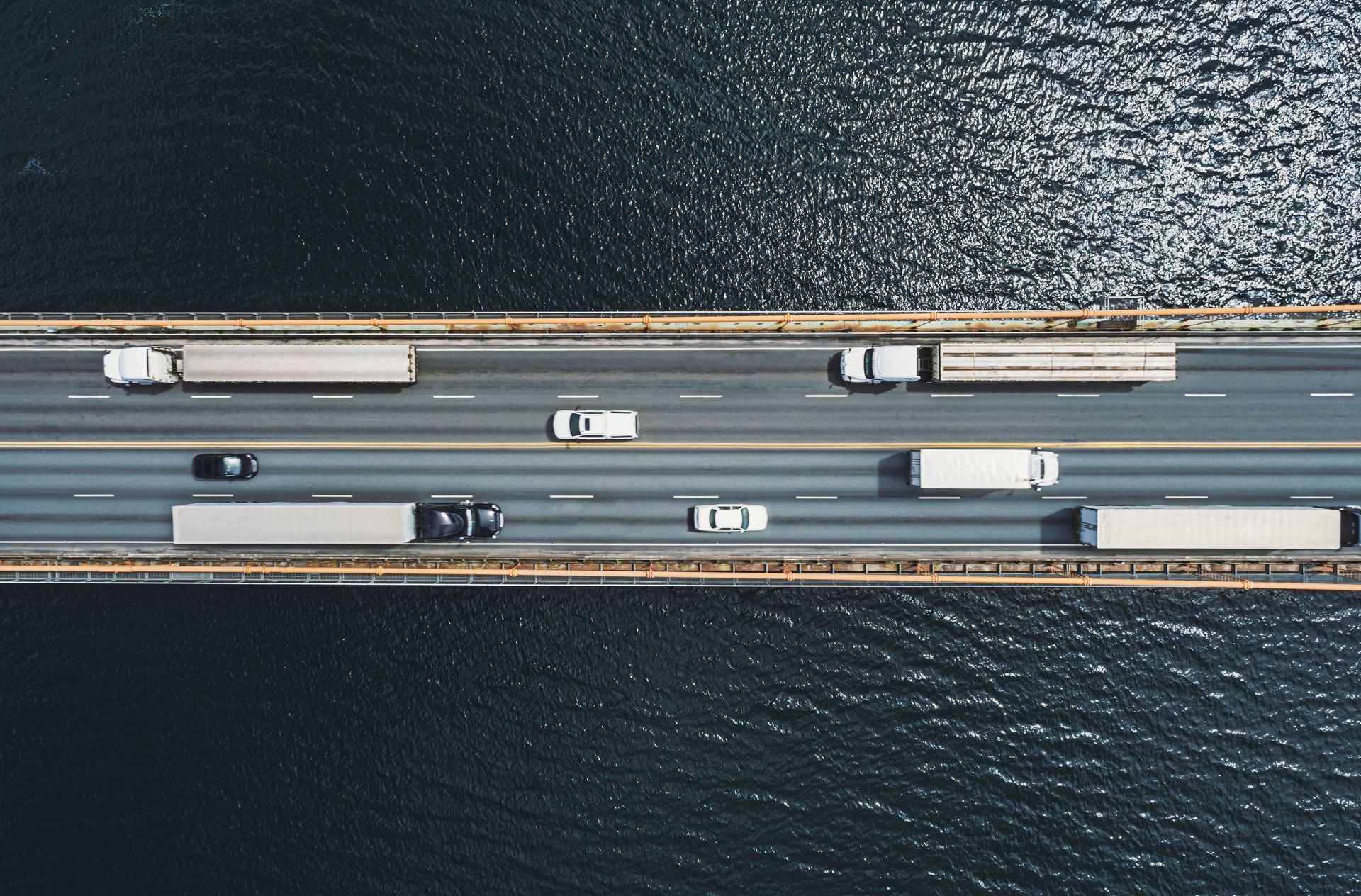 An aerial view of trucks driving on a bridge over a body of water.