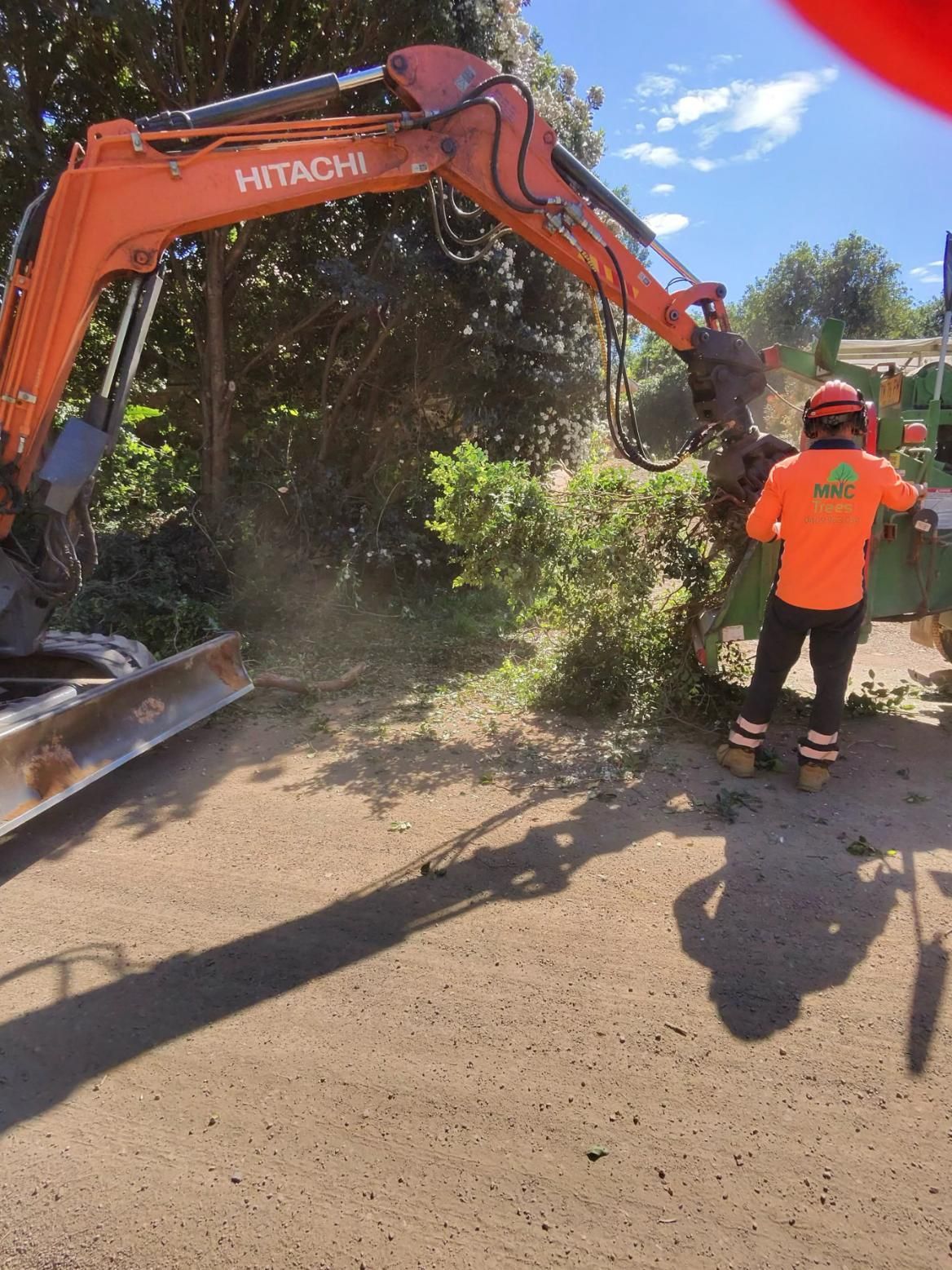 Orange Hitachi excavator clearing brush with worker in safety gear. — MNC Trees in Wauchope, NSW