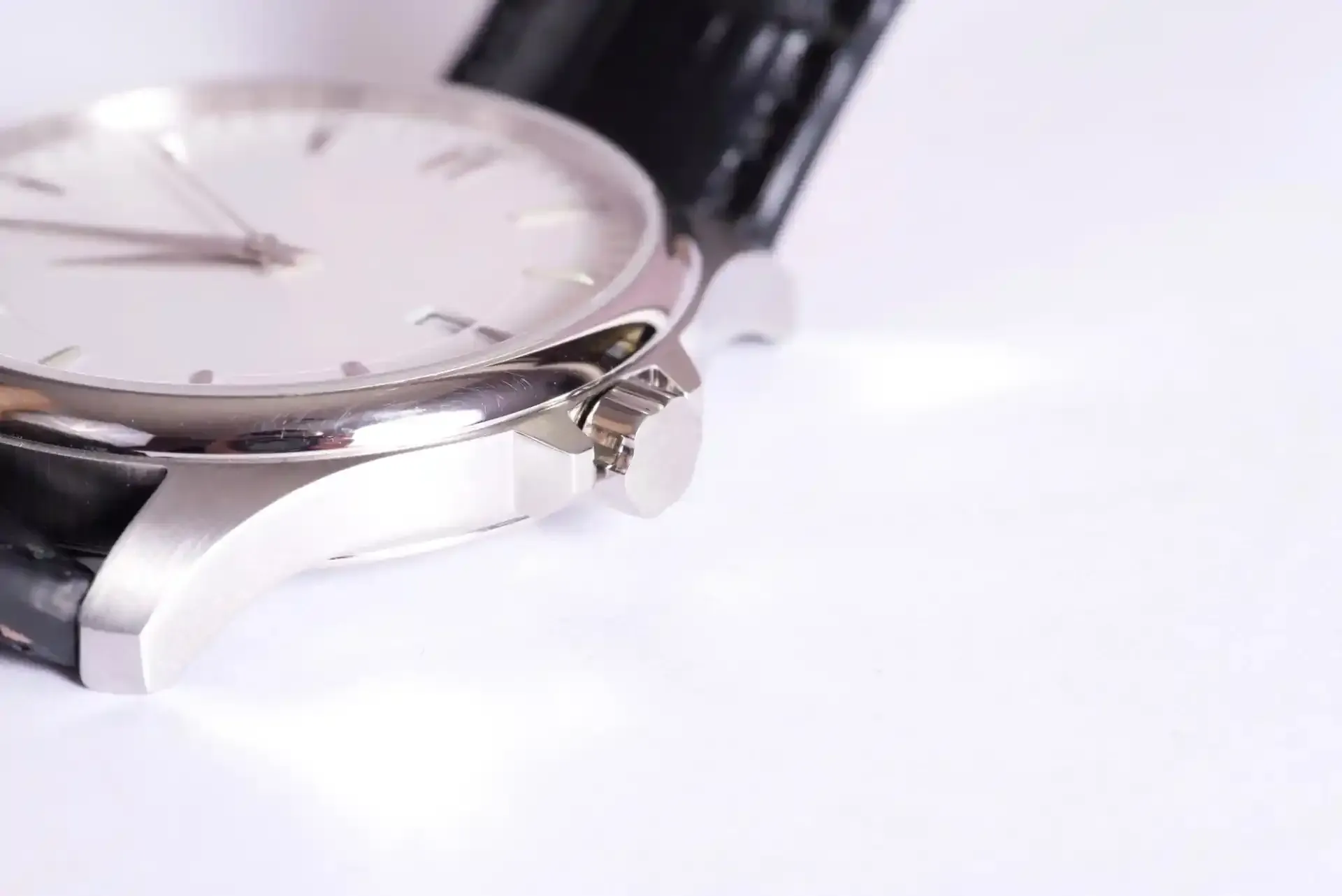 Primo piano di un orologio da polso argentato su una superficie bianca con cinturino in pelle nera.