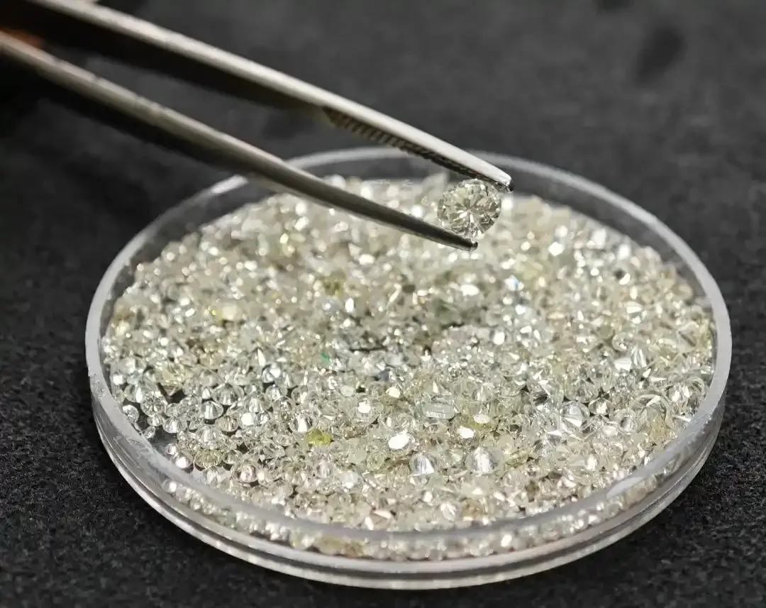 Pinzette che tengono un cristallo trasparente e scintillante sopra un piattino poco profondo contenente cristalli sfusi.