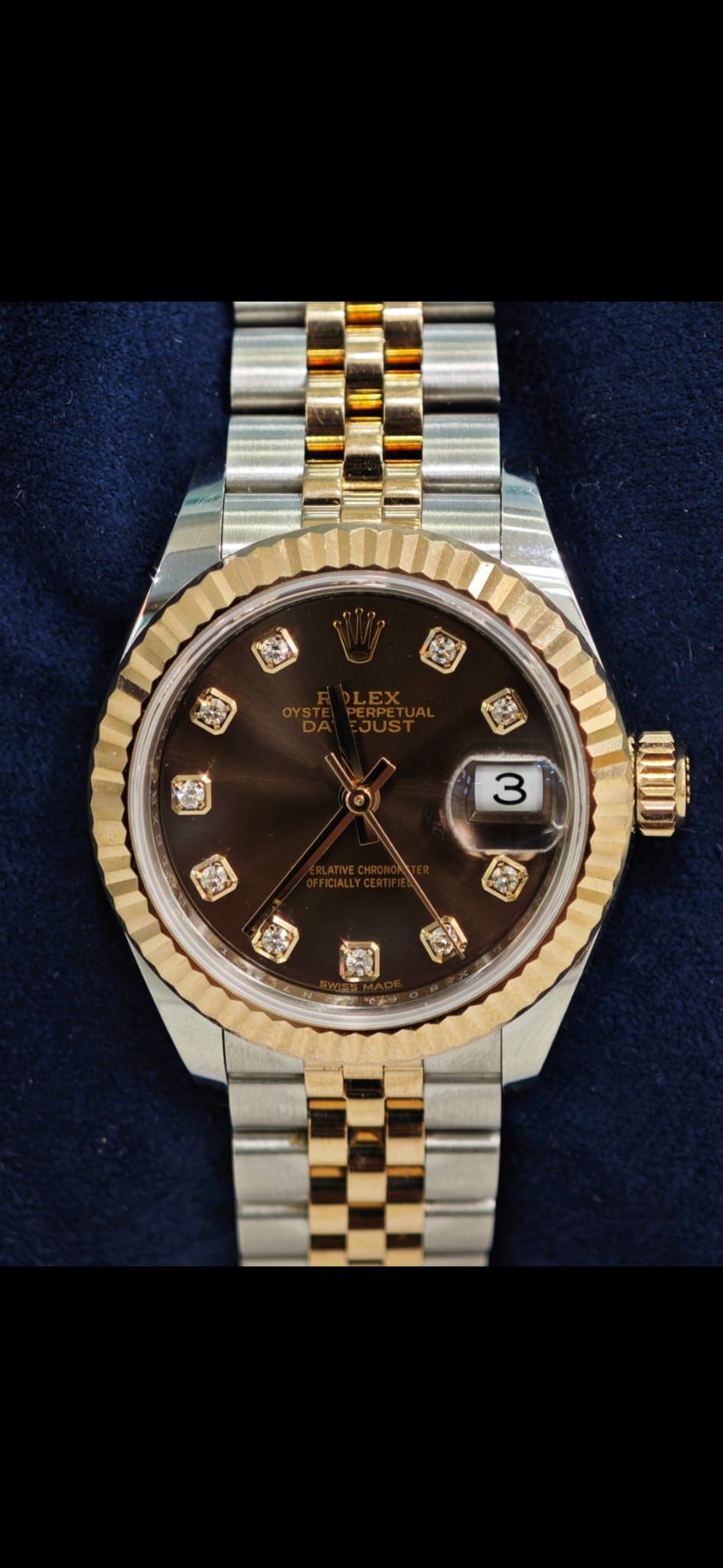 Orologio da polso bicolore oro e argento con quadrante marrone scuro e datario su sfondo blu.