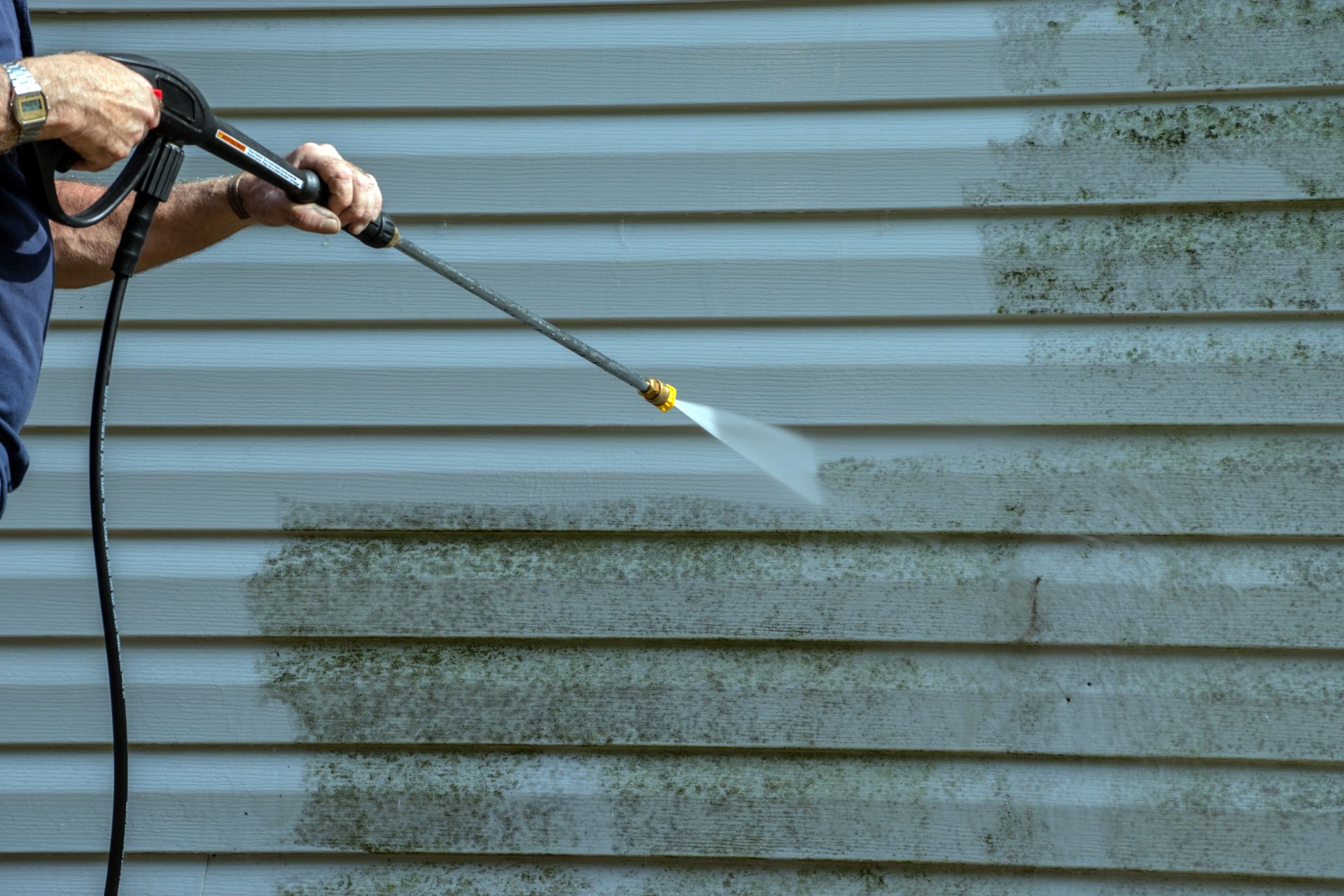 A man is using a high pressure washer to clean a siding
