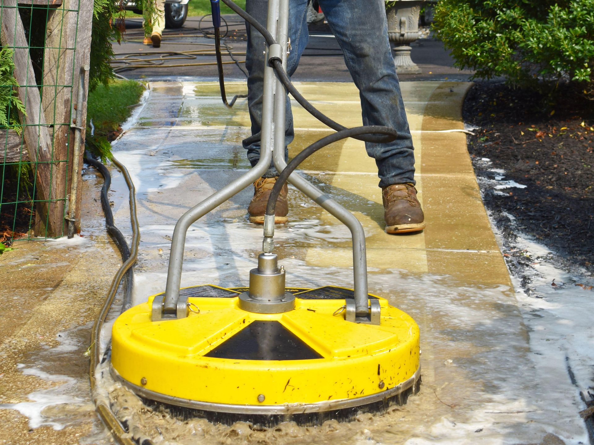 A man is using a yellow machine to clean a sidewalk.