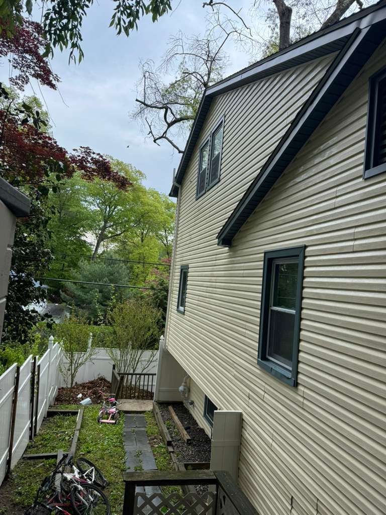 A man is cleaning the roof of a brick house with a high pressure washer.