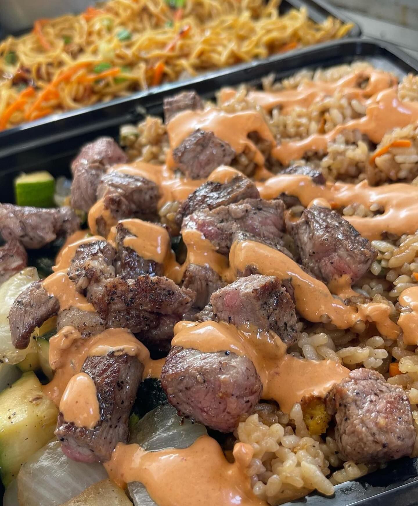 A close up of a tray of food with meat and rice on a table.