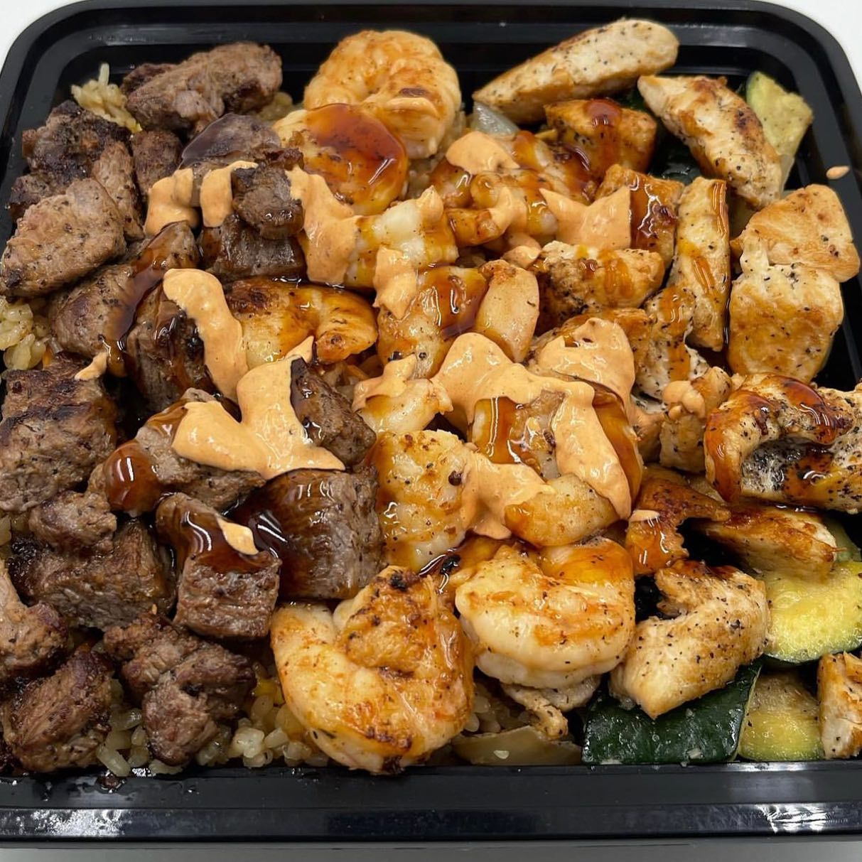 A black container filled with a variety of meats and vegetables.