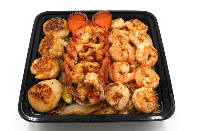 A black container filled with shrimp , scallops and rice.
