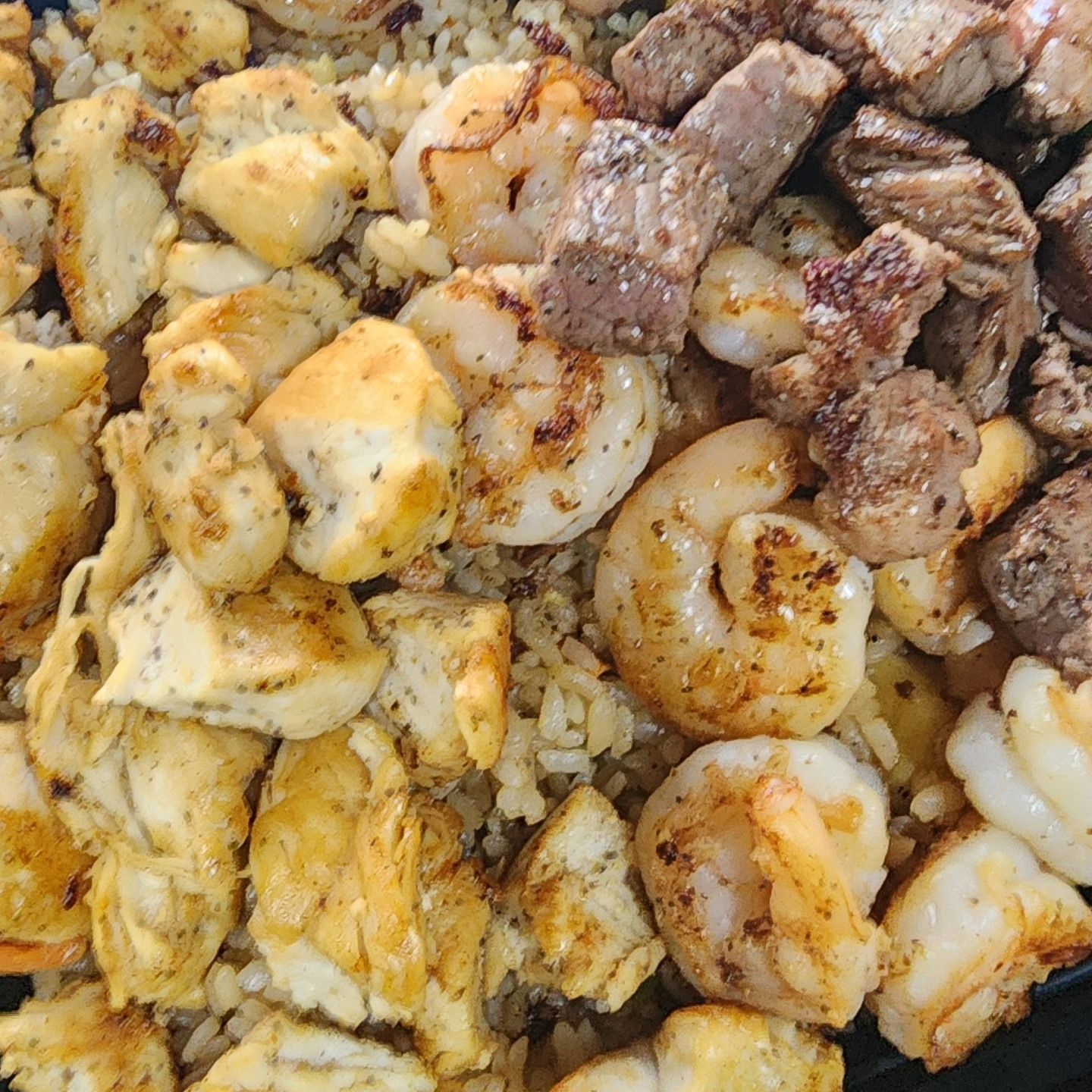 A close up of a plate of food with shrimp , rice and meat.
