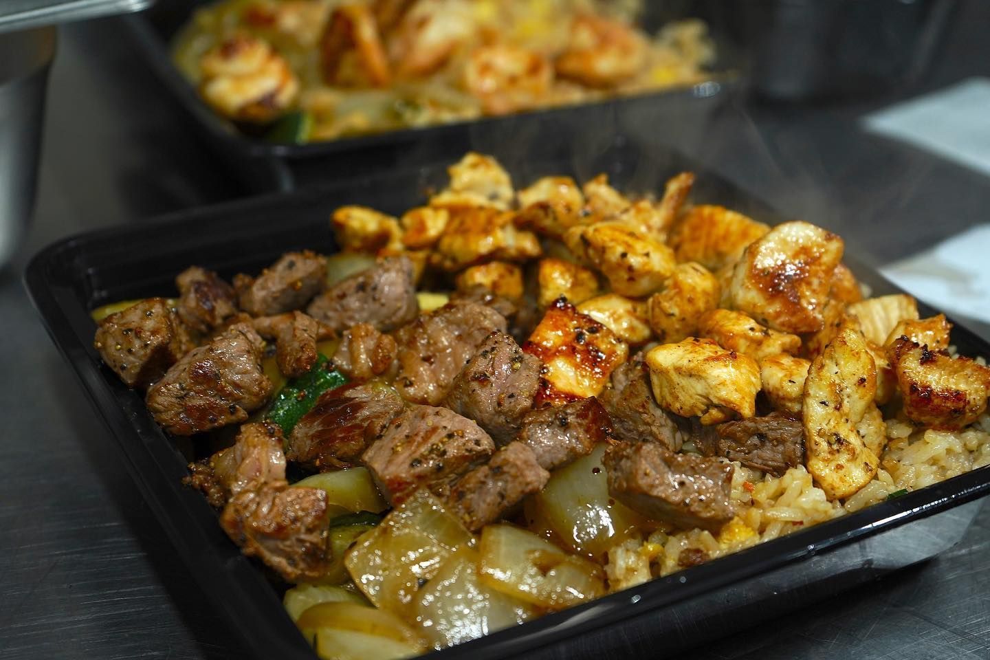 A close up of a tray of food with meat and rice on a table.