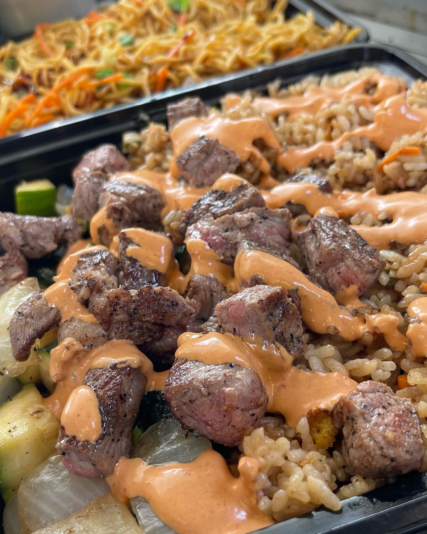 A close up of a tray of food with meat and rice on a table.