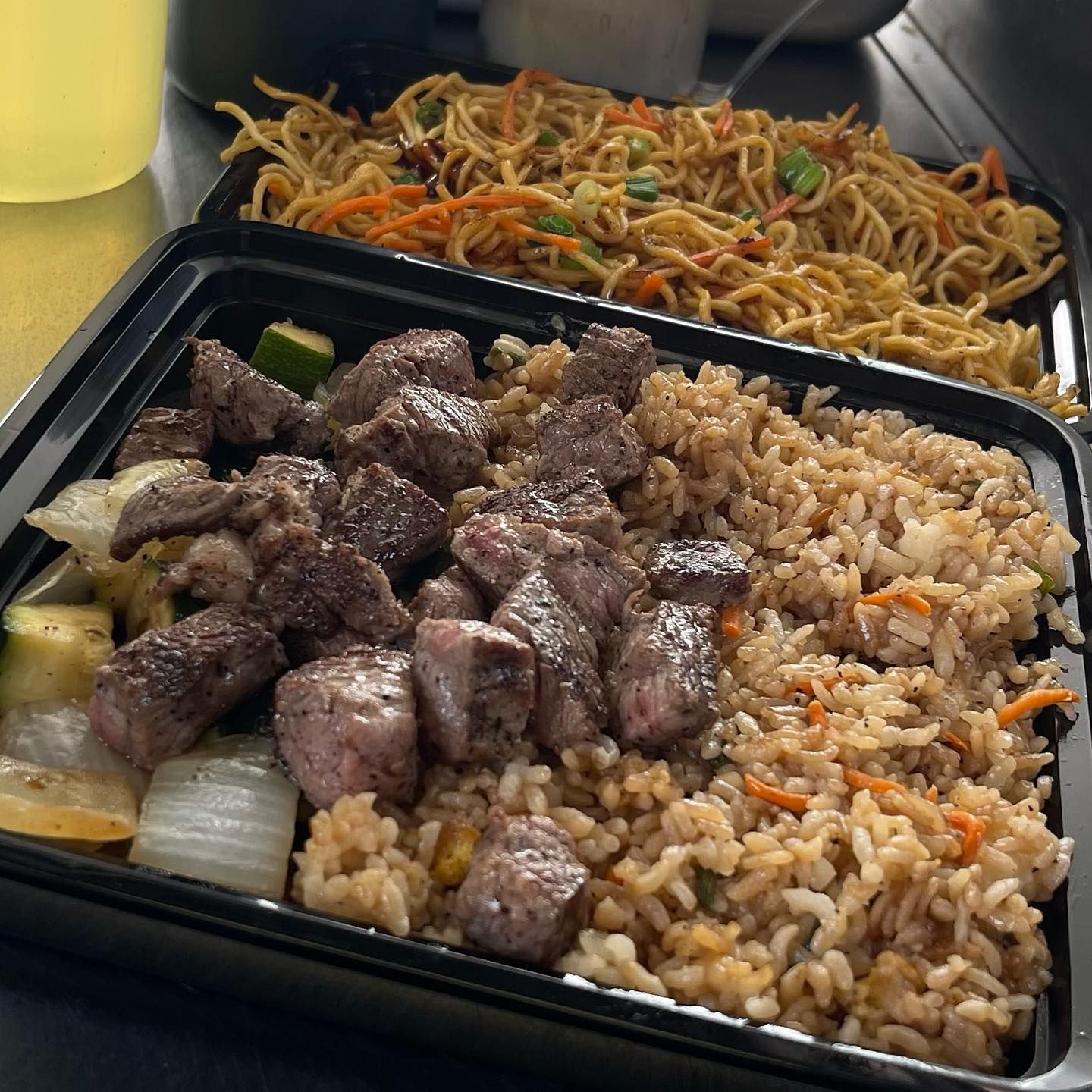 Two containers of food including rice and noodles on a table