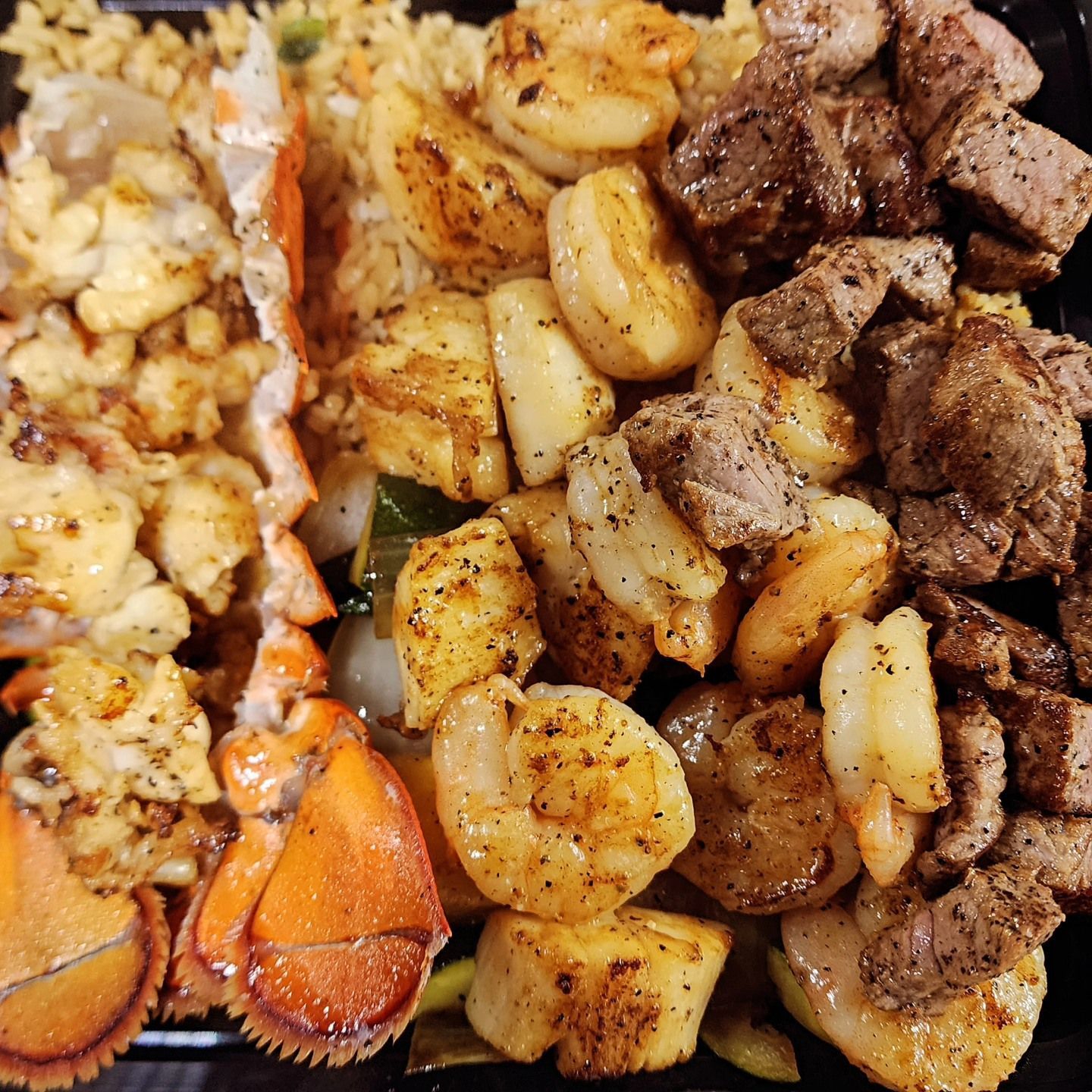 A close up of a plate of food with shrimp , meat and rice.