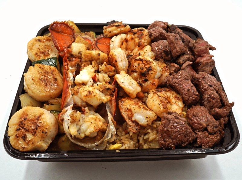 A tray of food with shrimp , steak , scallops and rice on a white background.