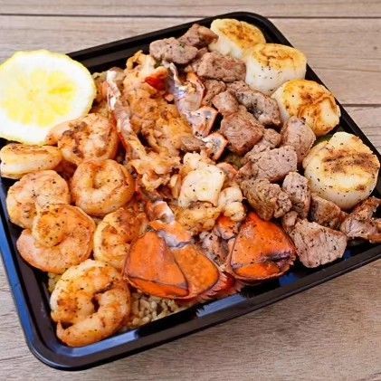 A black tray filled with shrimp , meat , scallops and rice.