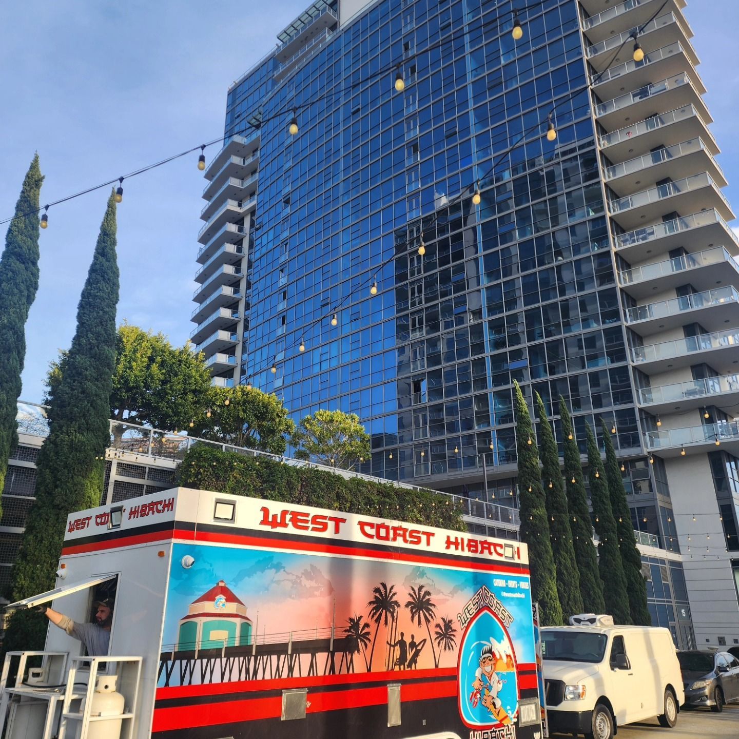 A west coast hot dog truck is parked in front of a tall building