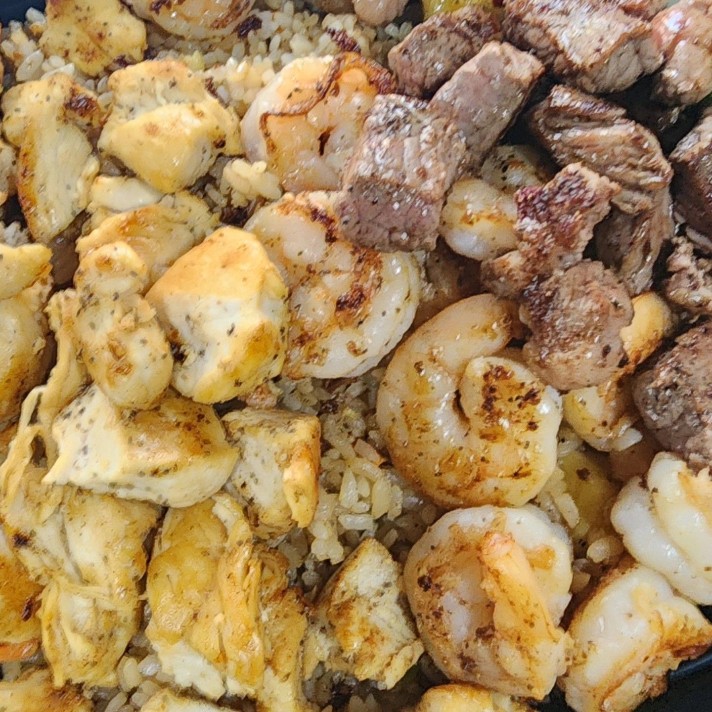 A close up of a plate of food with shrimp , steak and rice.