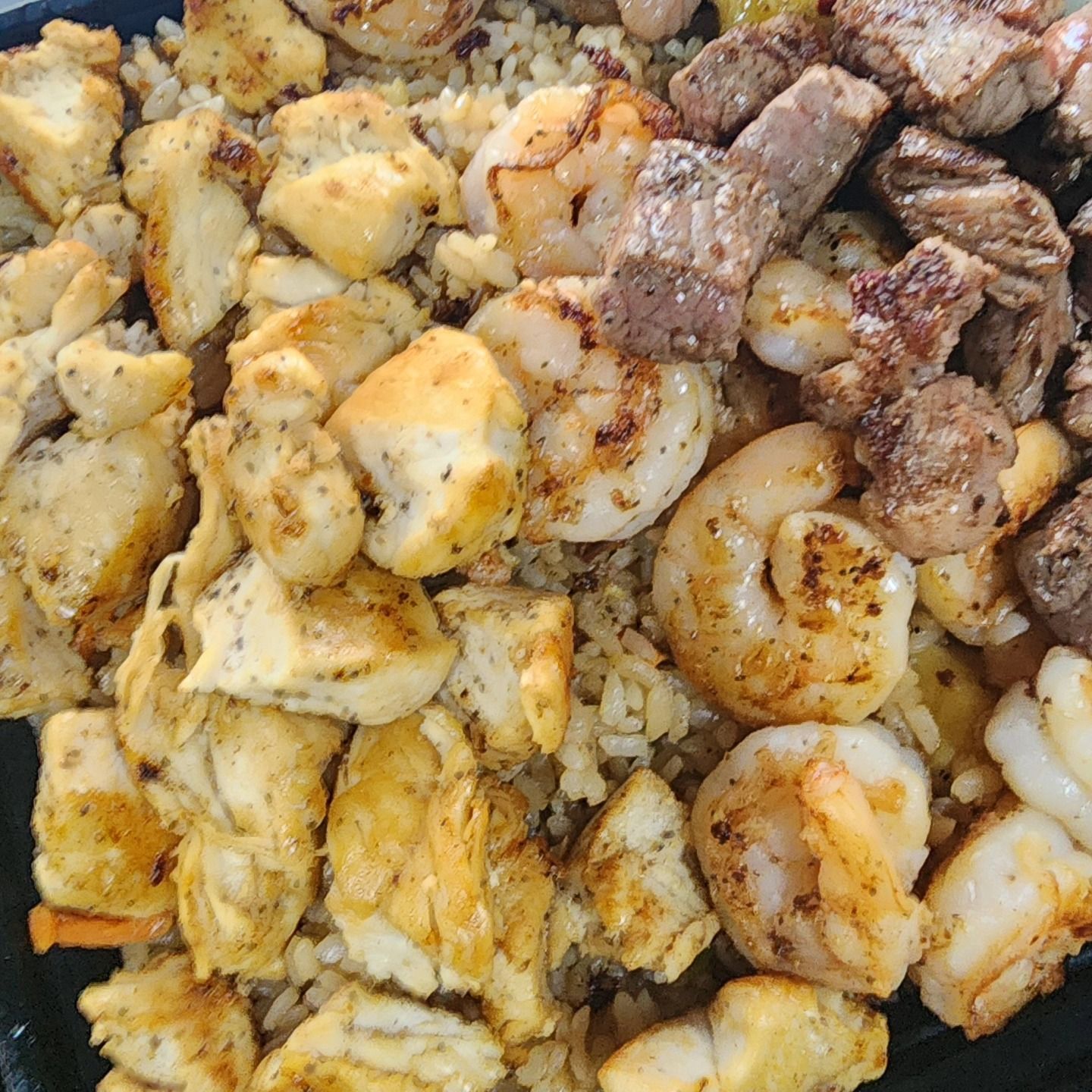 A close up of a plate of food with shrimp , steak and rice.