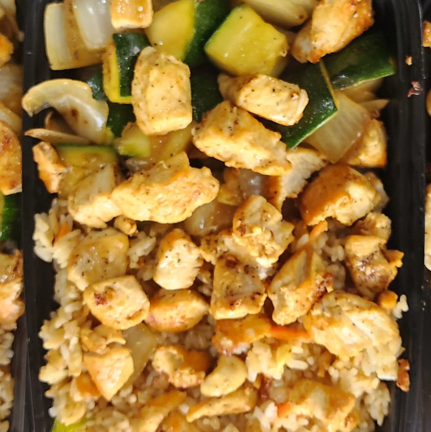 A black container filled with chicken and rice