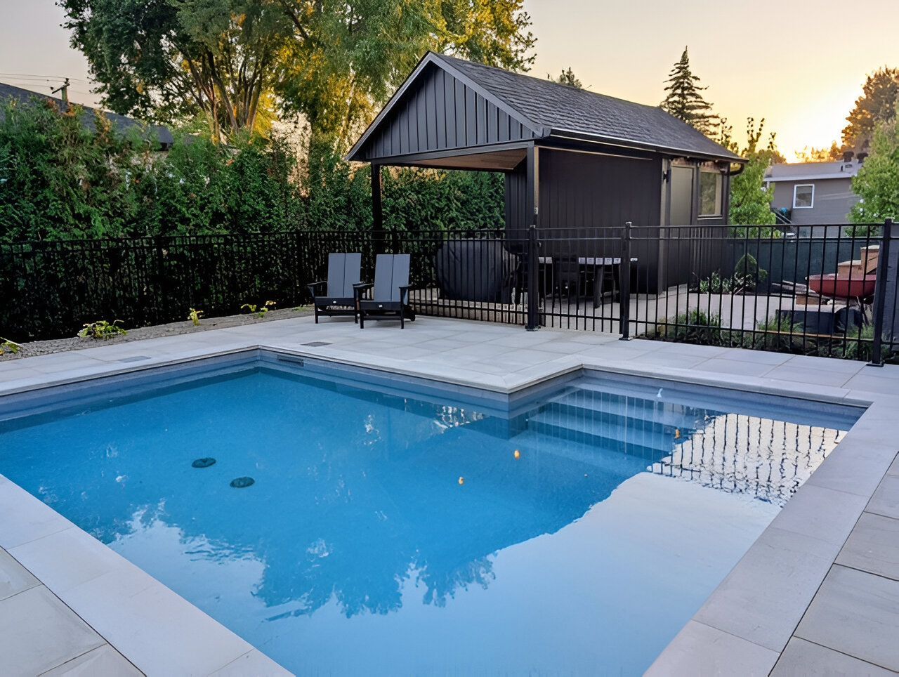 Backyard pool with steps, lounge chairs, and a dark-painted pergola. Surrounded by a black fence and greenery.