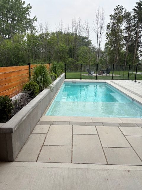 Rectangular pool with light blue water, surrounded by grey stone patio and a wooden fence.