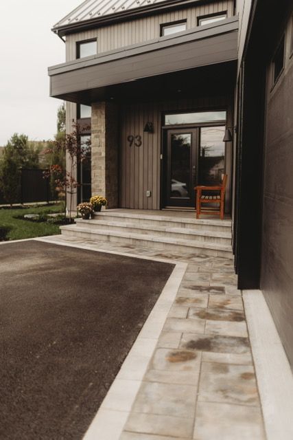 Modern home exterior with steps leading to the front door, asphalt driveway, and stone pathway.