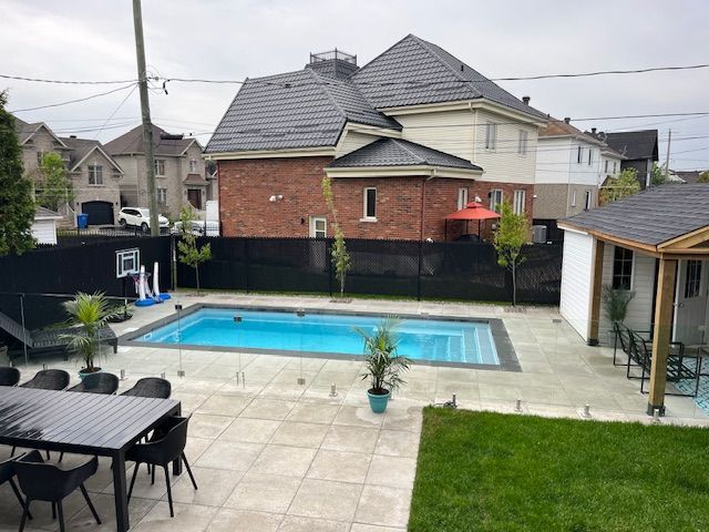 Backyard with a rectangular pool, patio, black fence, and a two-story brick house with a dark gray roof.