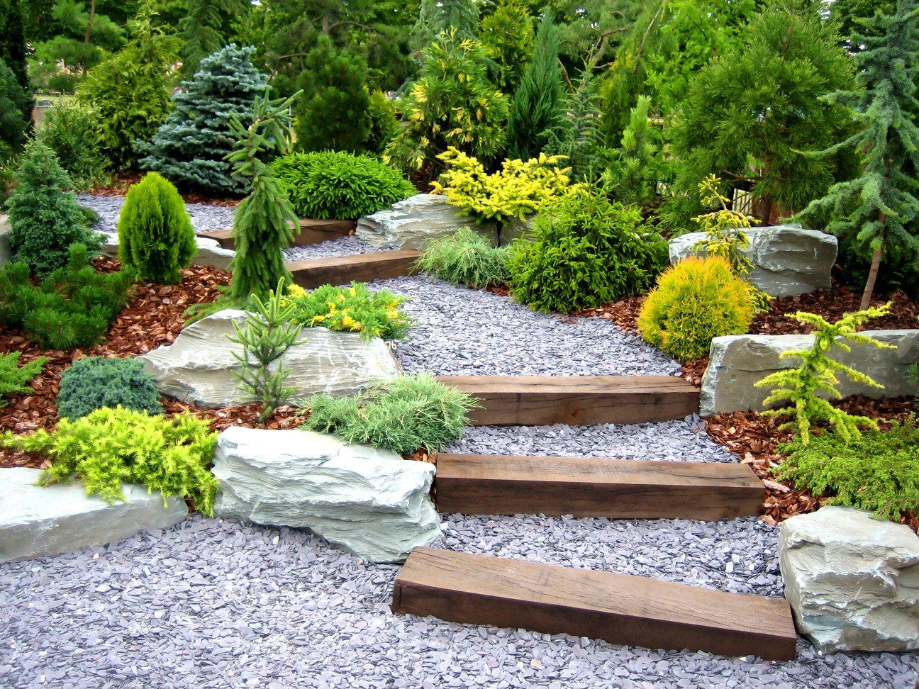 Un jardin avec des escaliers et des rochers entouré d'arbres et d'arbustes.
