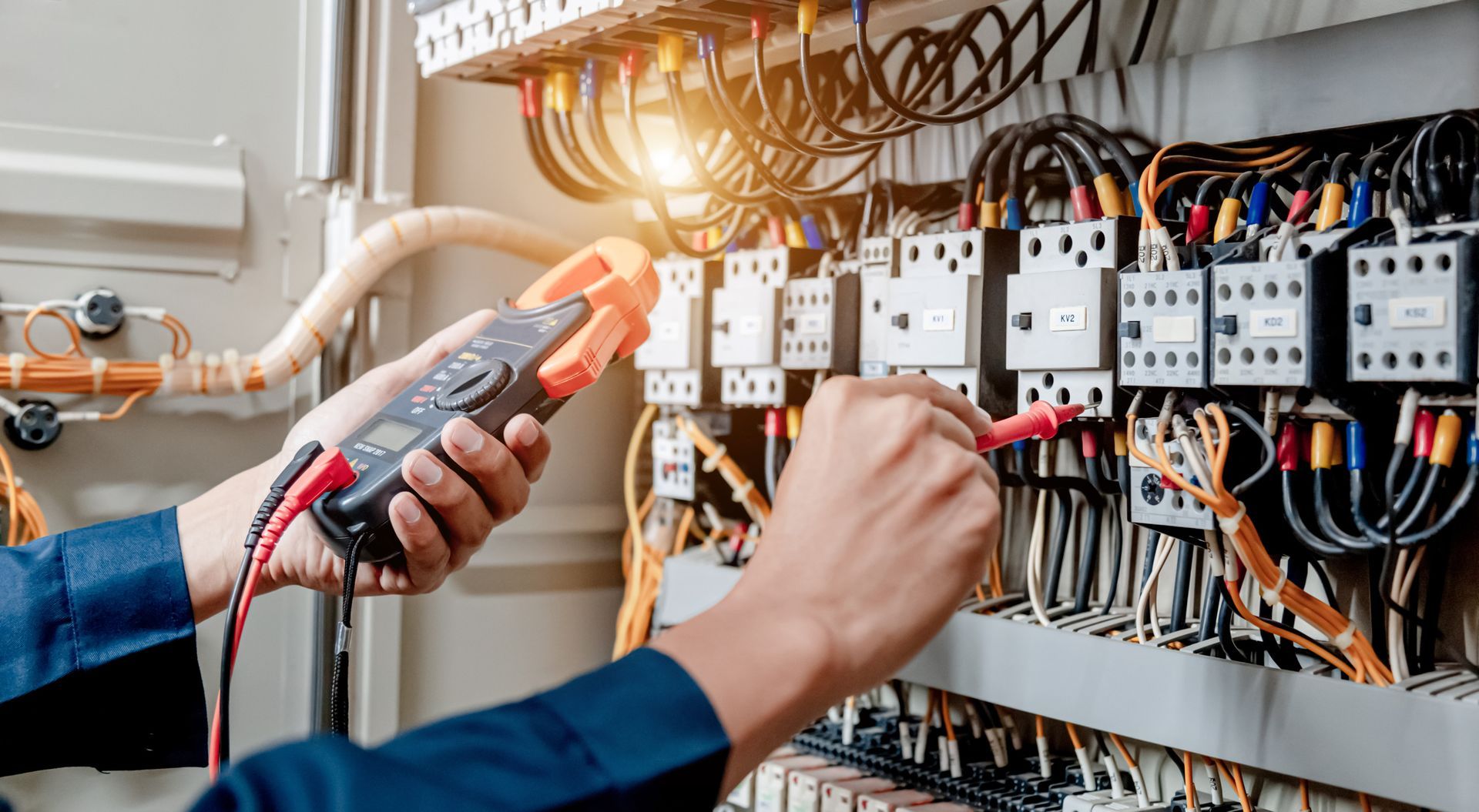 An electrician is working on an electrical panel with a clamp meter.