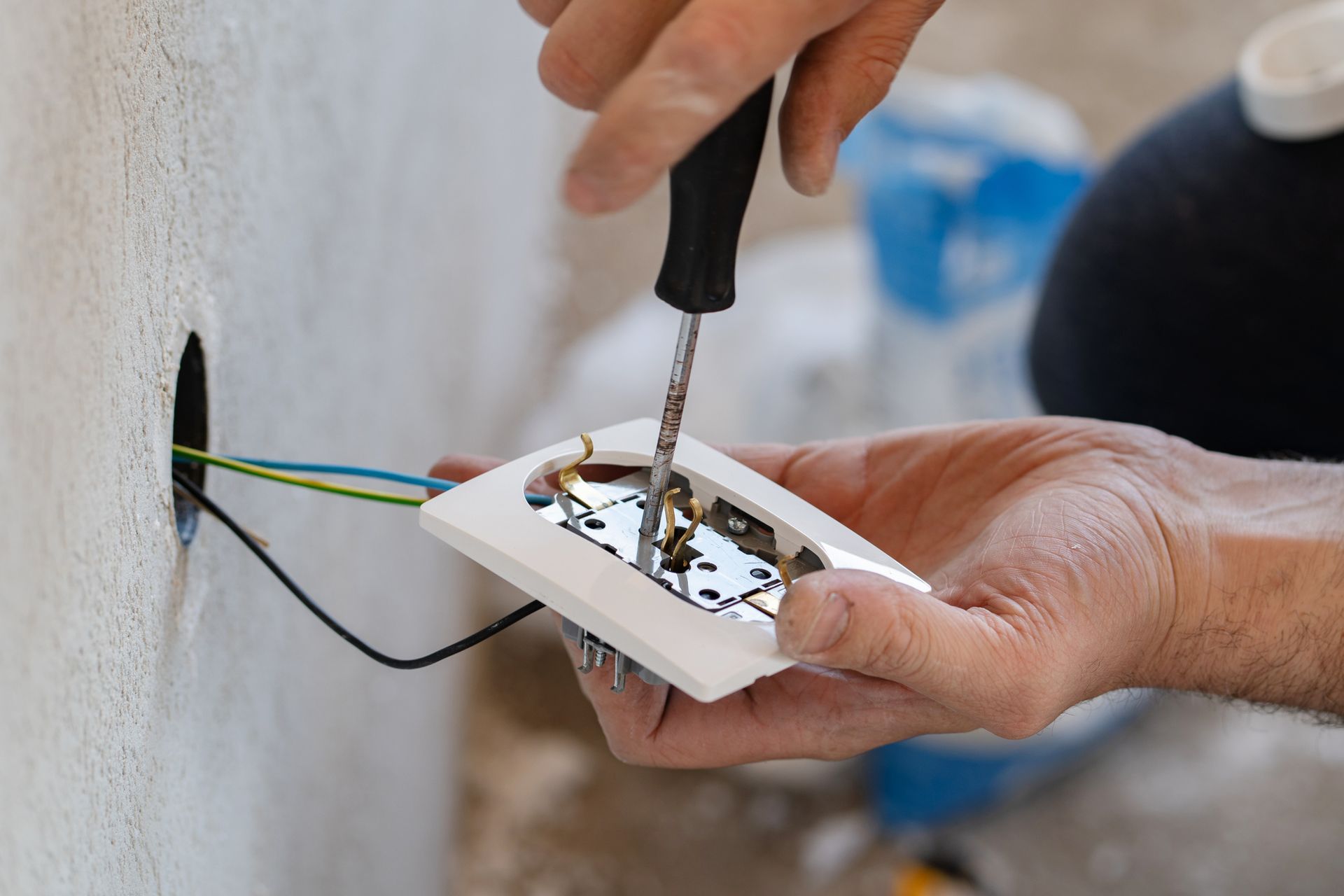 A person is fixing an electrical outlet with a screwdriver.