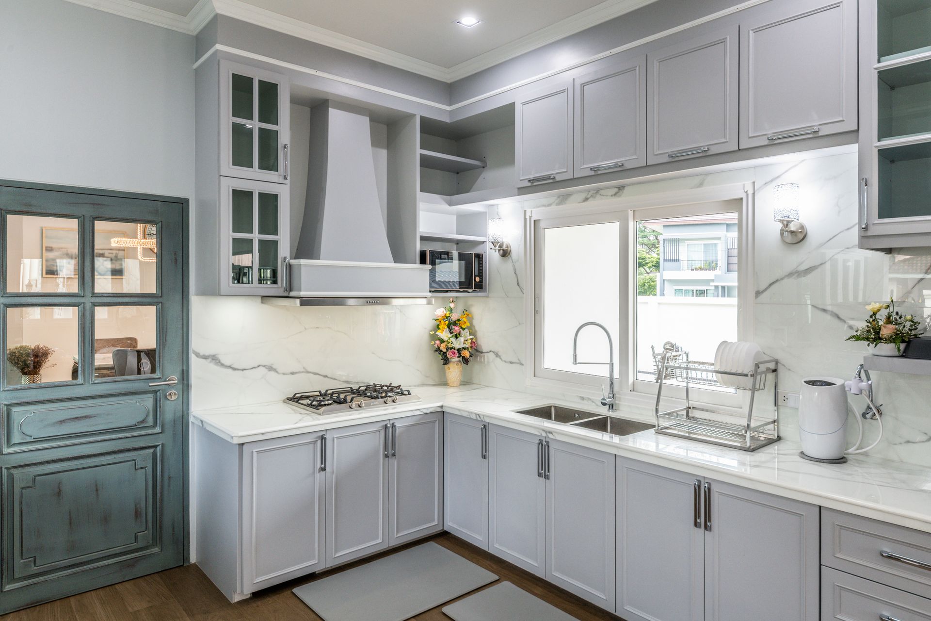 A kitchen with gray cabinets , white counter tops, a sink, and a window.