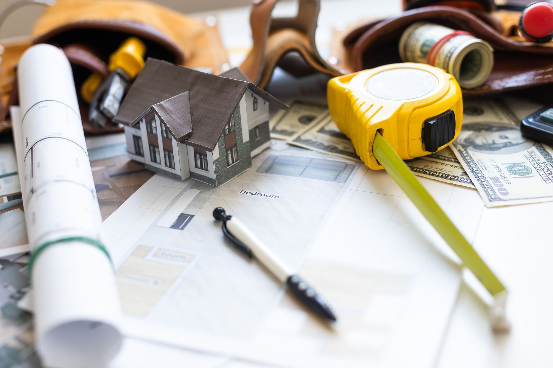 A model house is sitting on top of a table next to a tape measure. A model house is sitting on top of a table next to a tape measure.