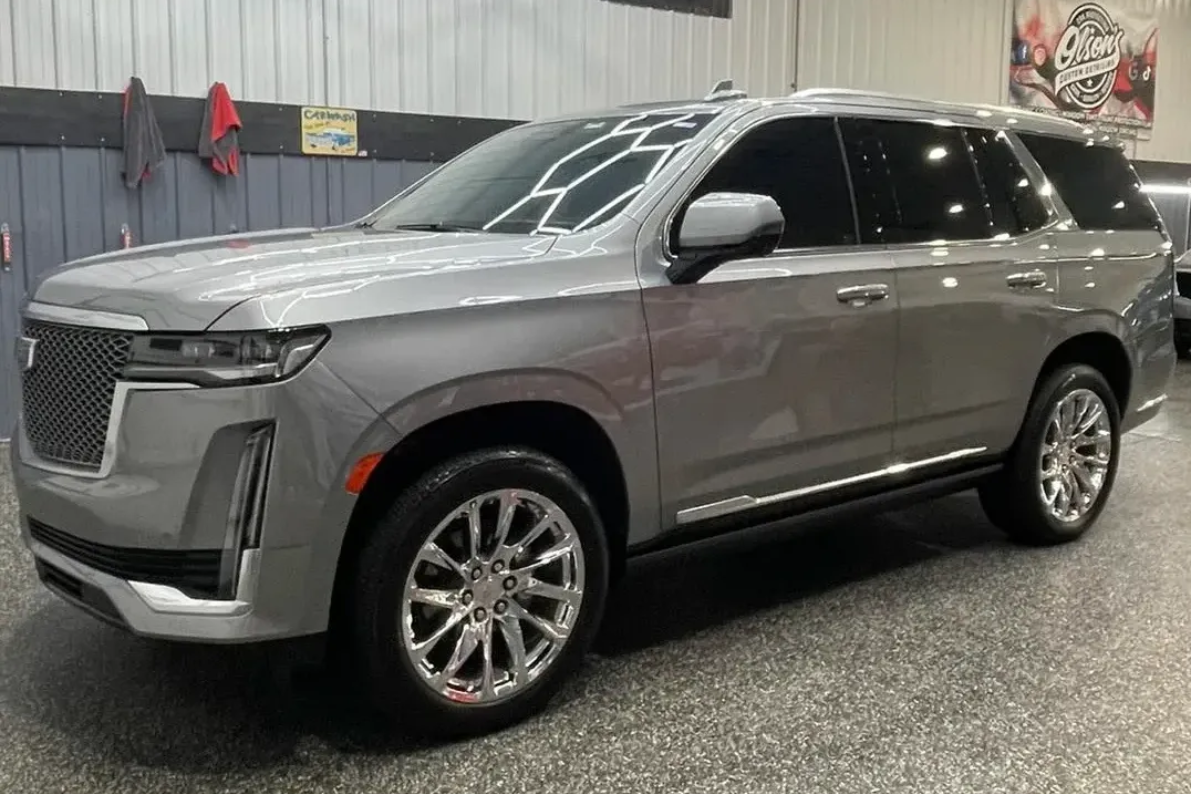 Silver Cadillac Escalade SUV parked indoors with tinted windows.