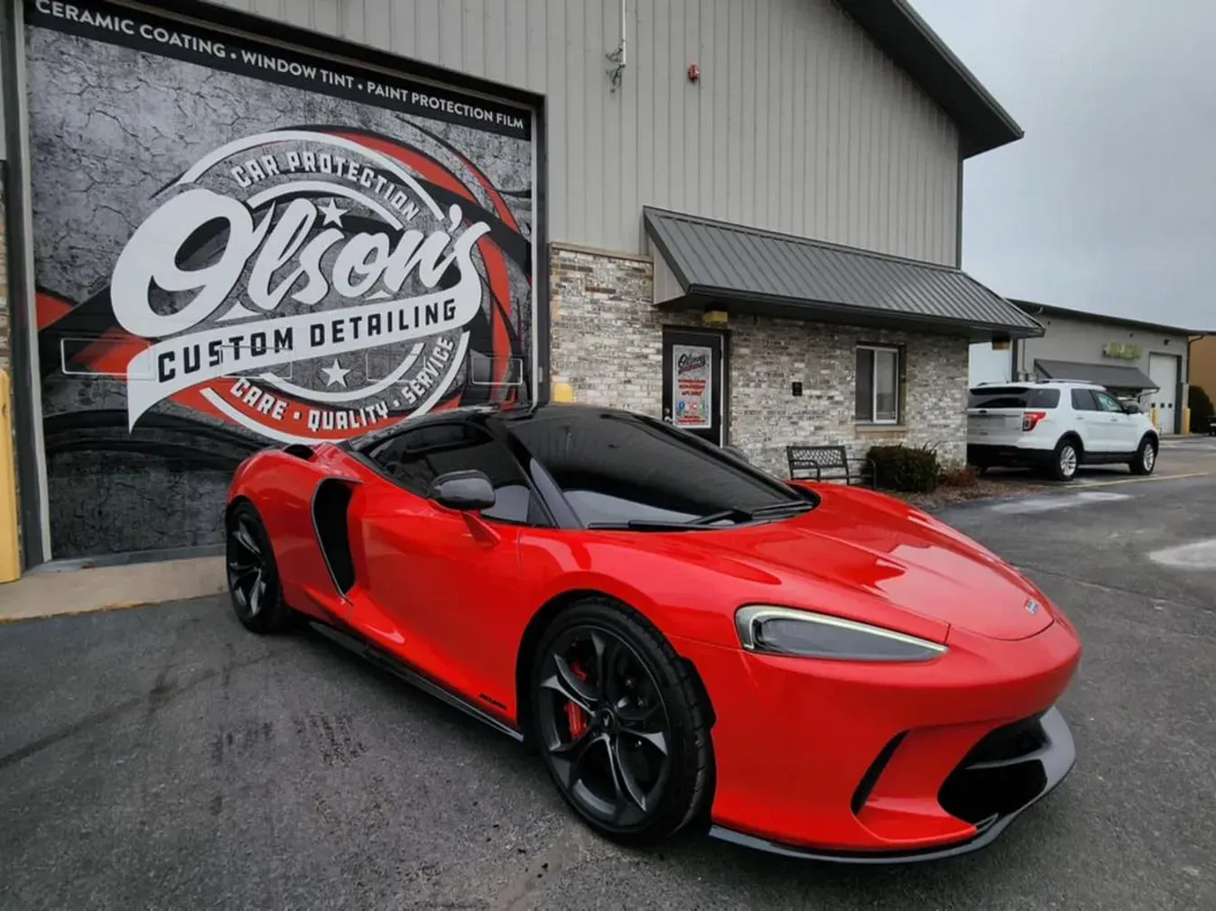 Red sports car parked outside a custom detailing shop with a large logo mural on the wall