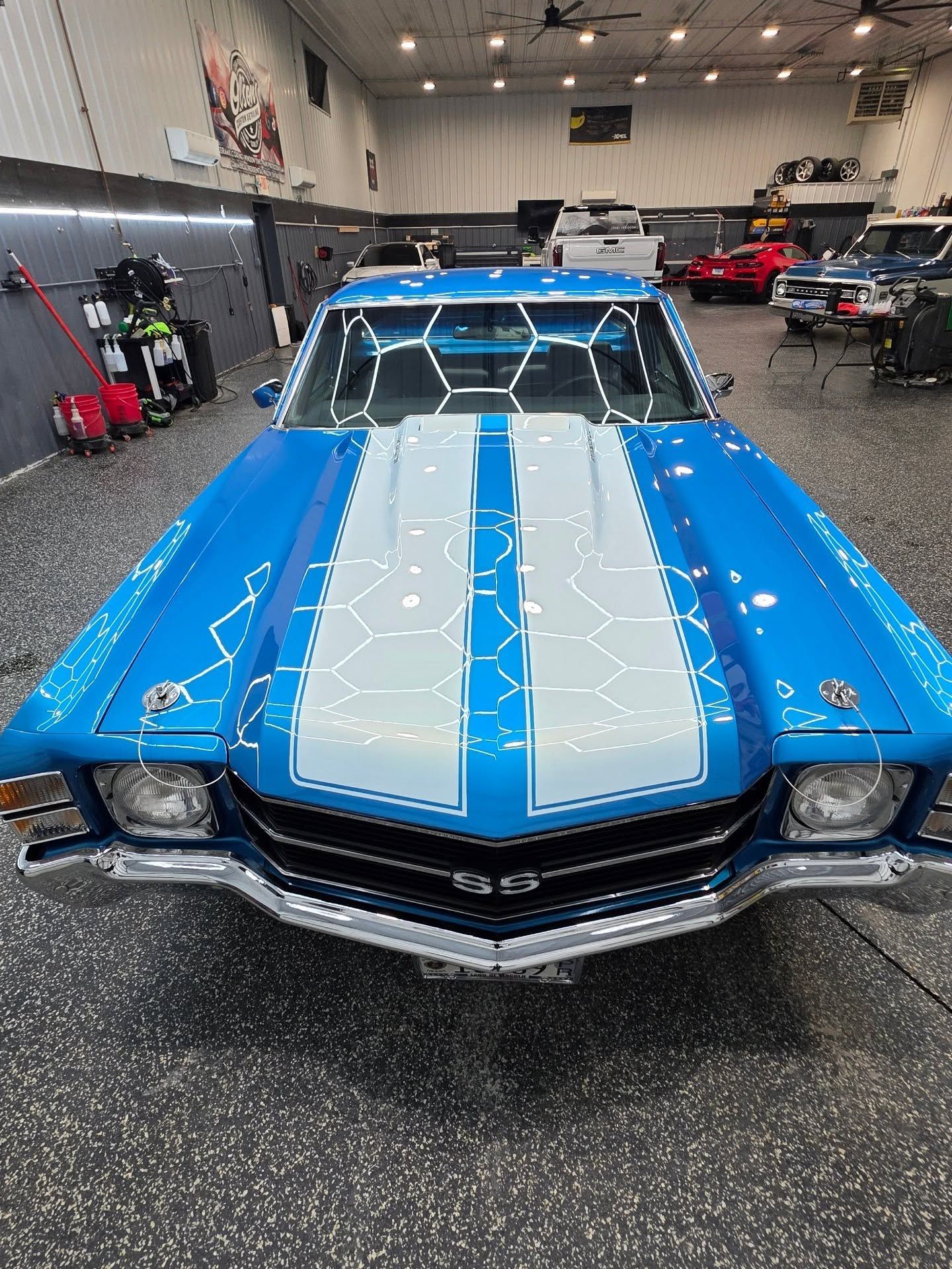 Blue classic car with silver racing stripes displayed indoors in a garage showroom