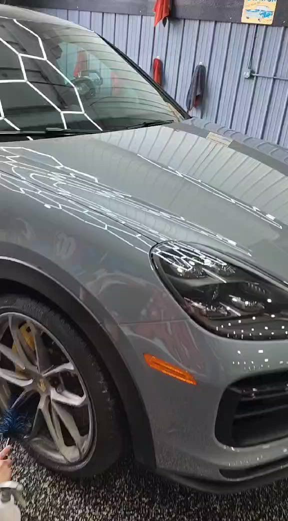 A man applies protective film to the front of a gray Acura. He is kneeling near the car, with spray bottle.