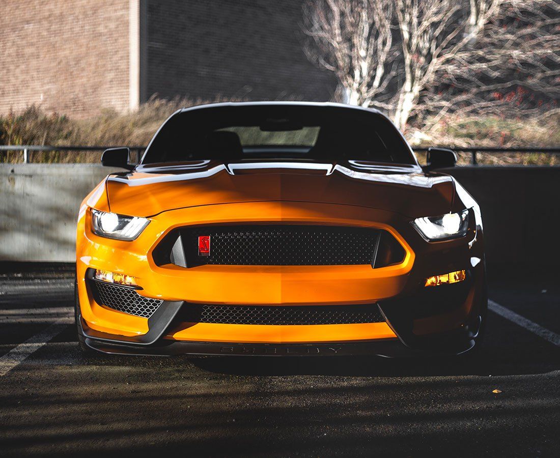 Orange sports car parked at night with headlights on, viewed from the front.