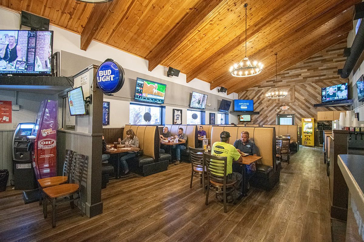Restaurant bar area with TVs, wooden ceiling, and seated patrons watching sports