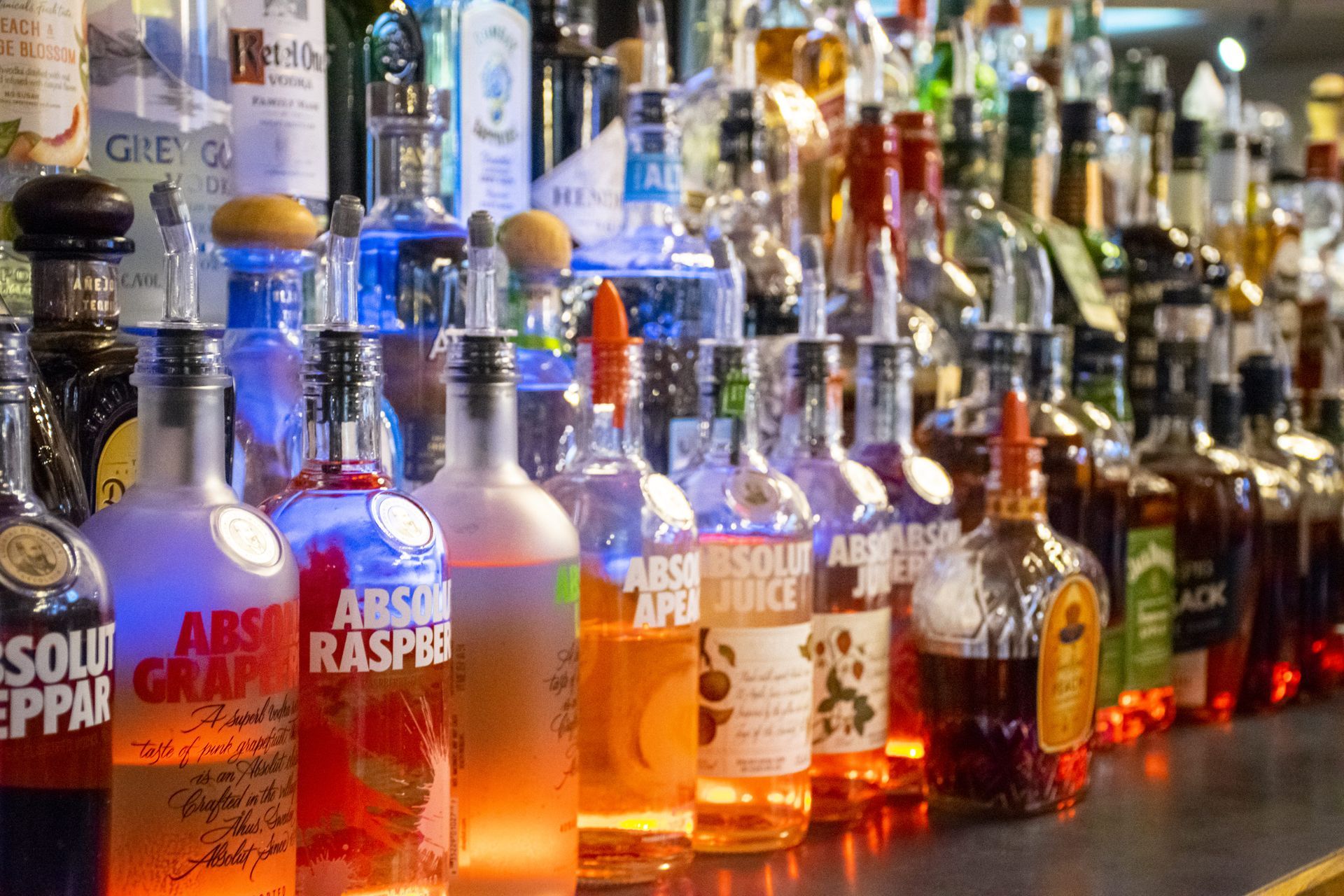 Rows of assorted liquor bottles lit by colorful bar lights on a counter