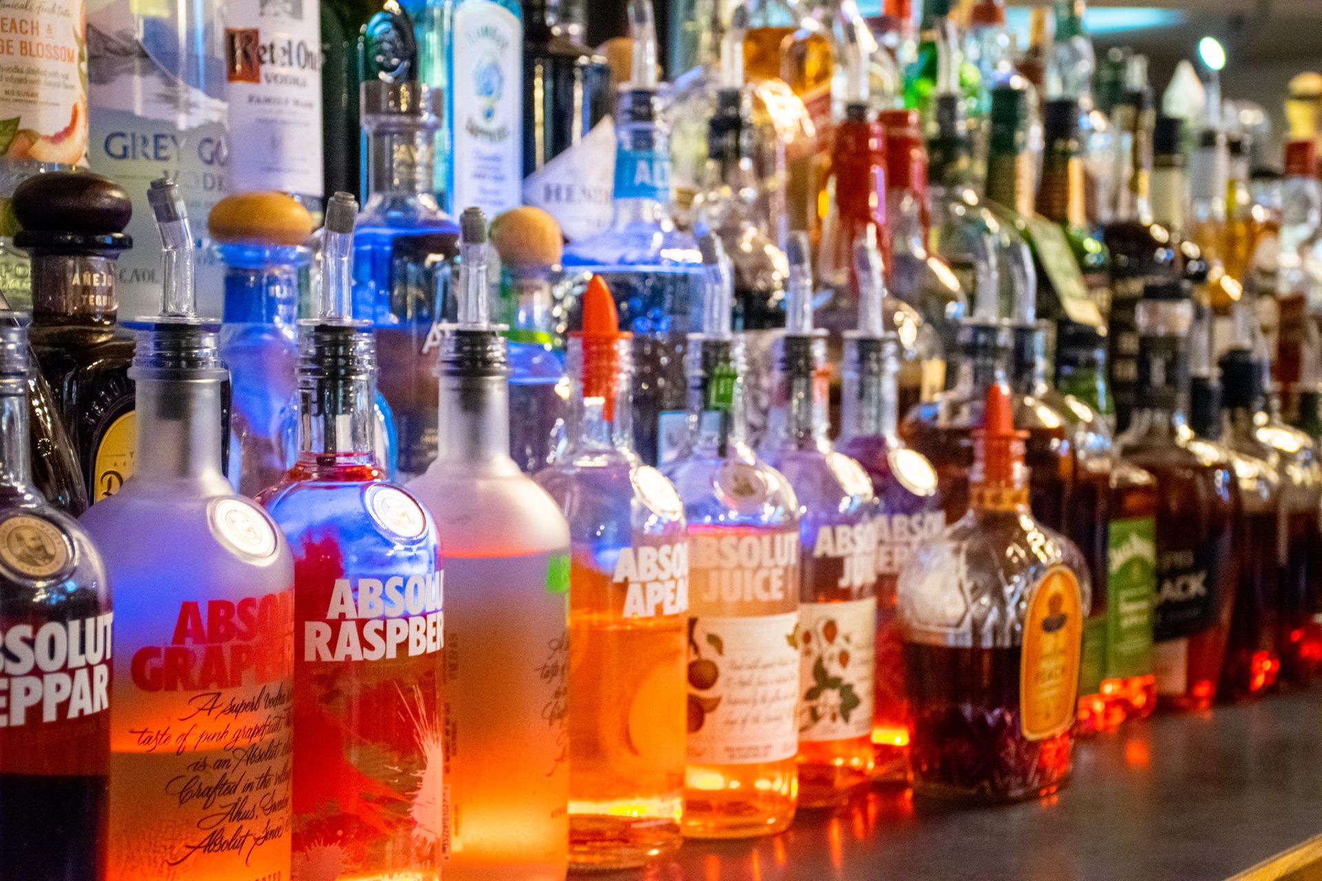 Assorted liquor bottles lined up on a bar counter with colorful reflections