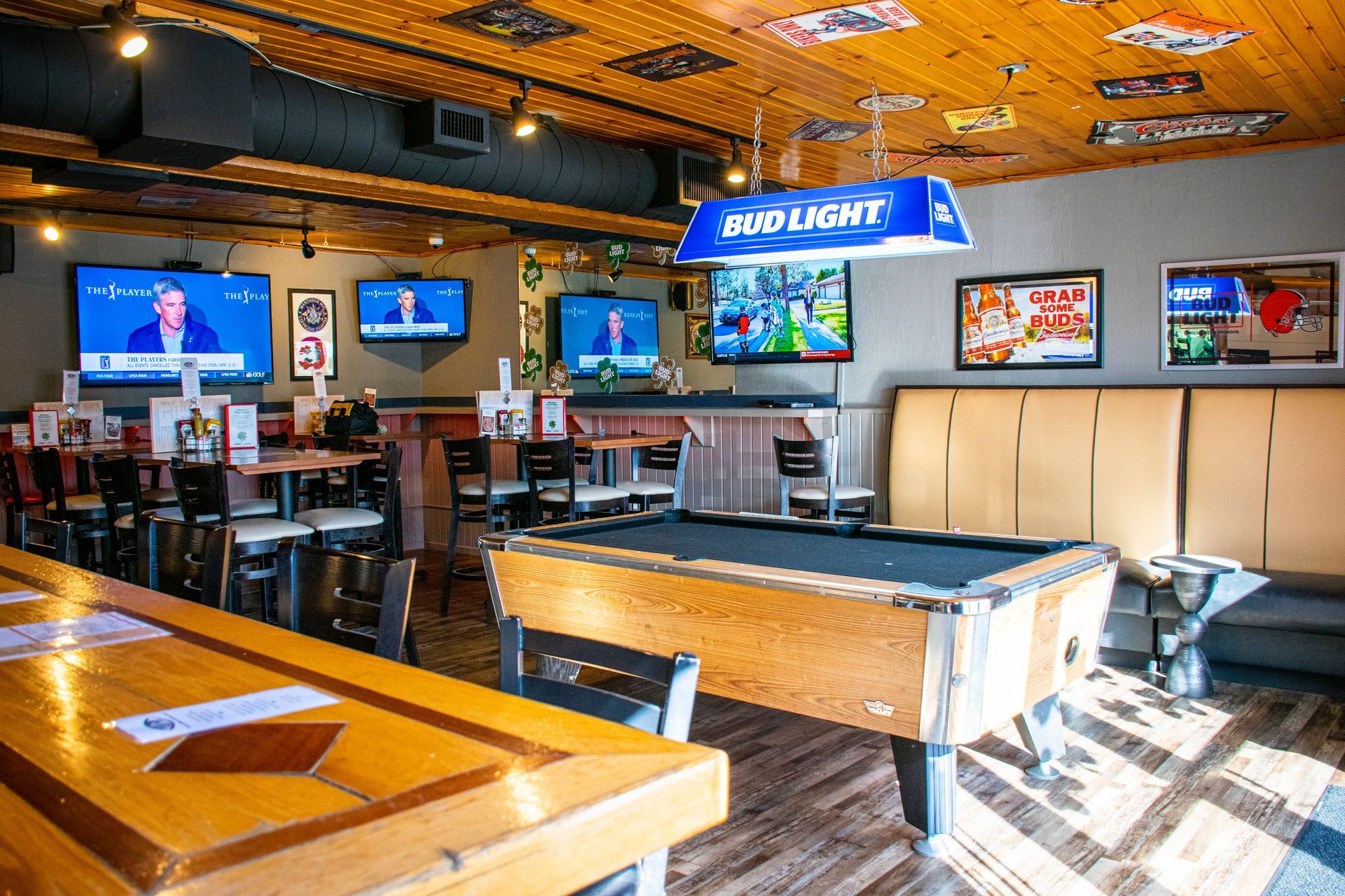Empty sports bar with pool tables, TV screens, and Bud Light signs, lit by warm orange ceiling lights