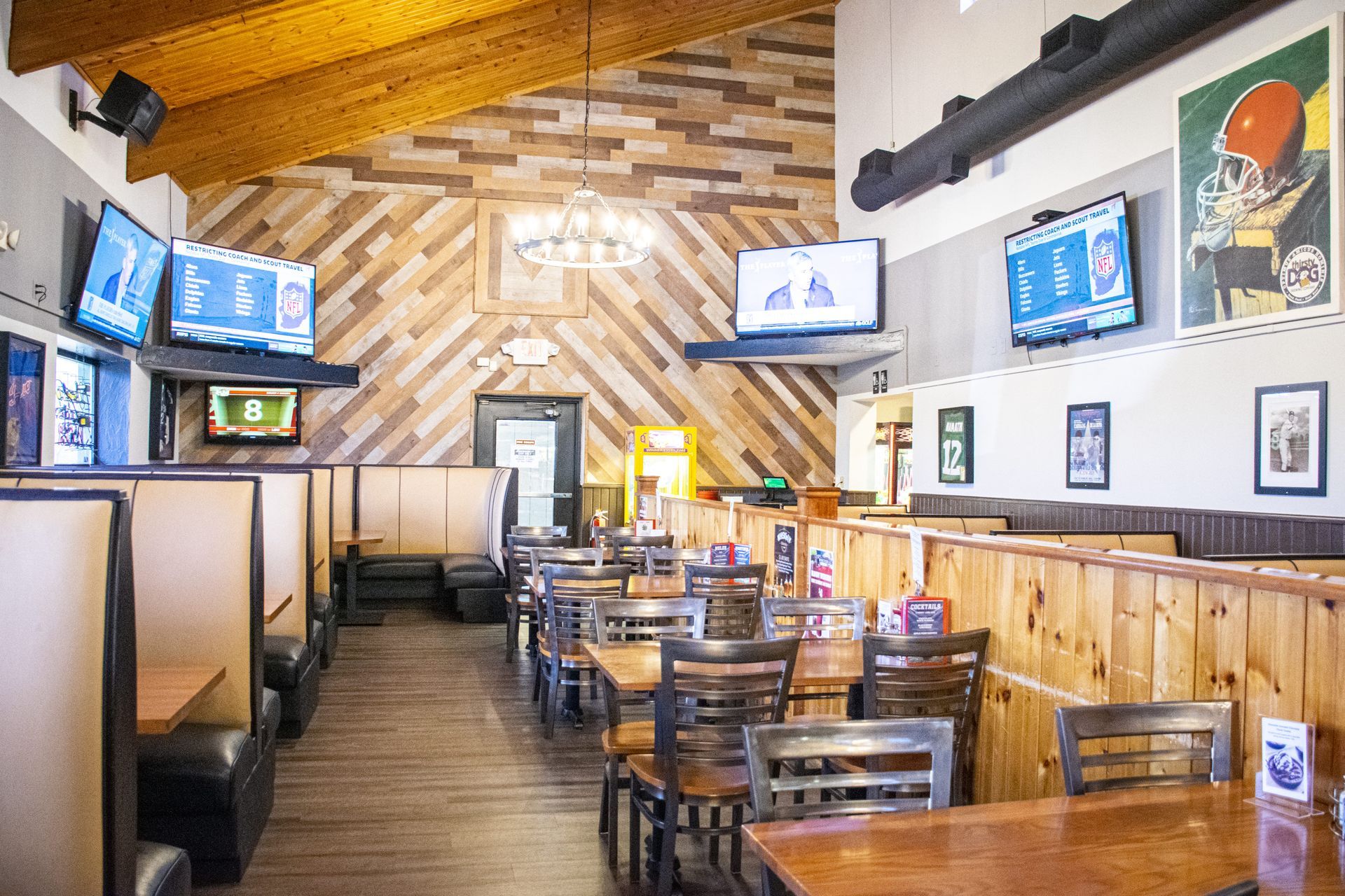 Empty restaurant dining room with wooden tables, booths, wall-mounted TVs, and framed sports decor.