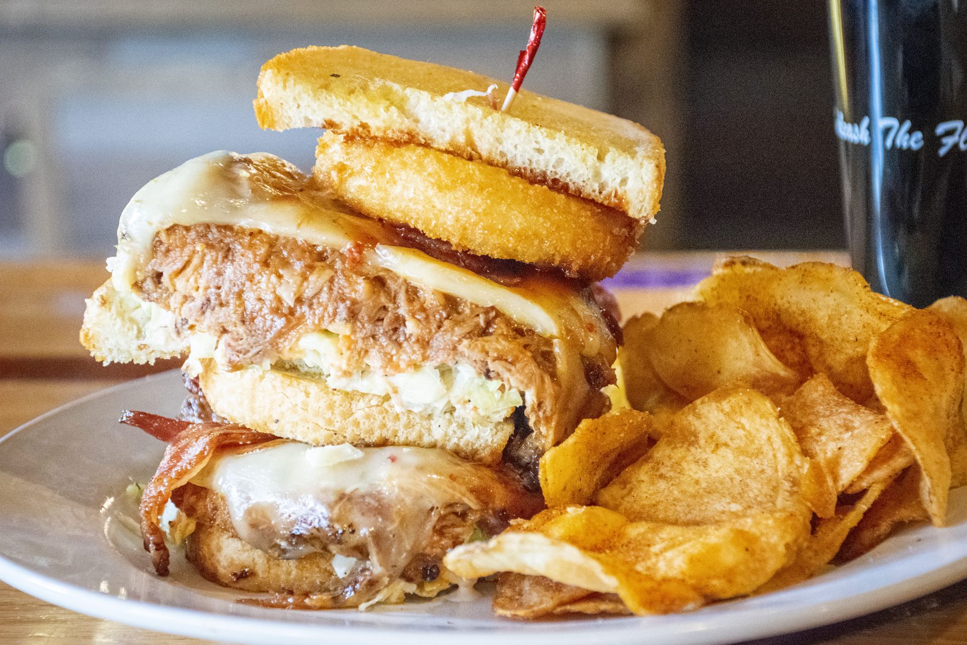 Stacked burger with onion rings and potato chips on a plate