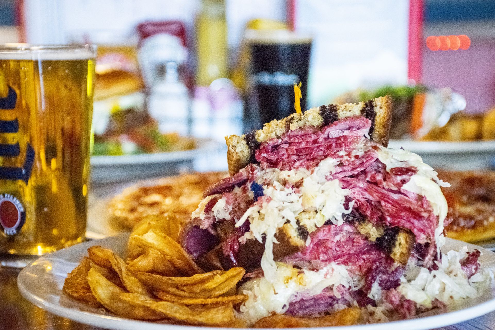 Heaped pastrami sandwich with fries and a beer on a restaurant table