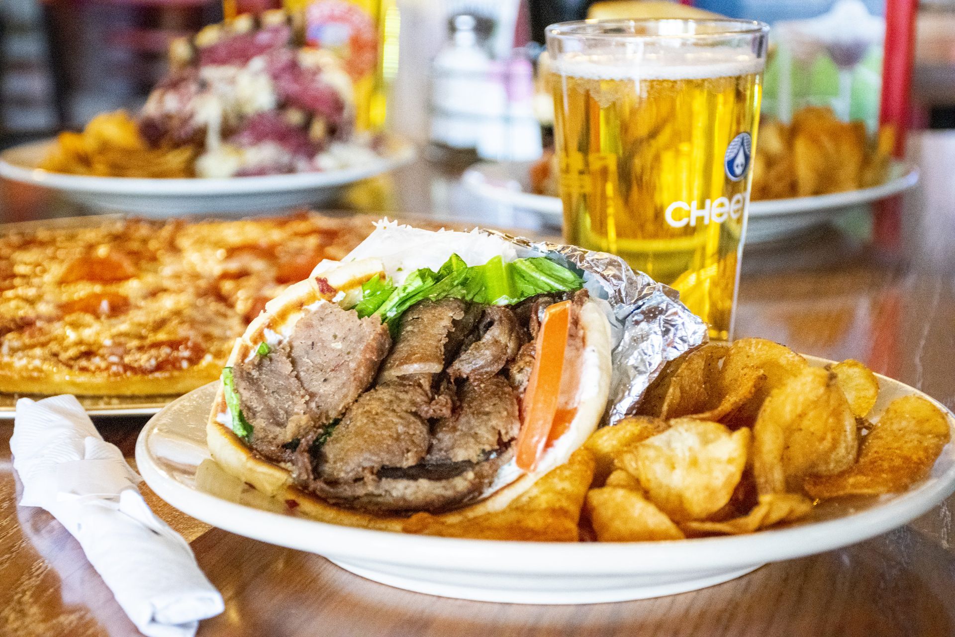 Plate of sliced meat sandwich, fries, and beer on a table in a restaurant