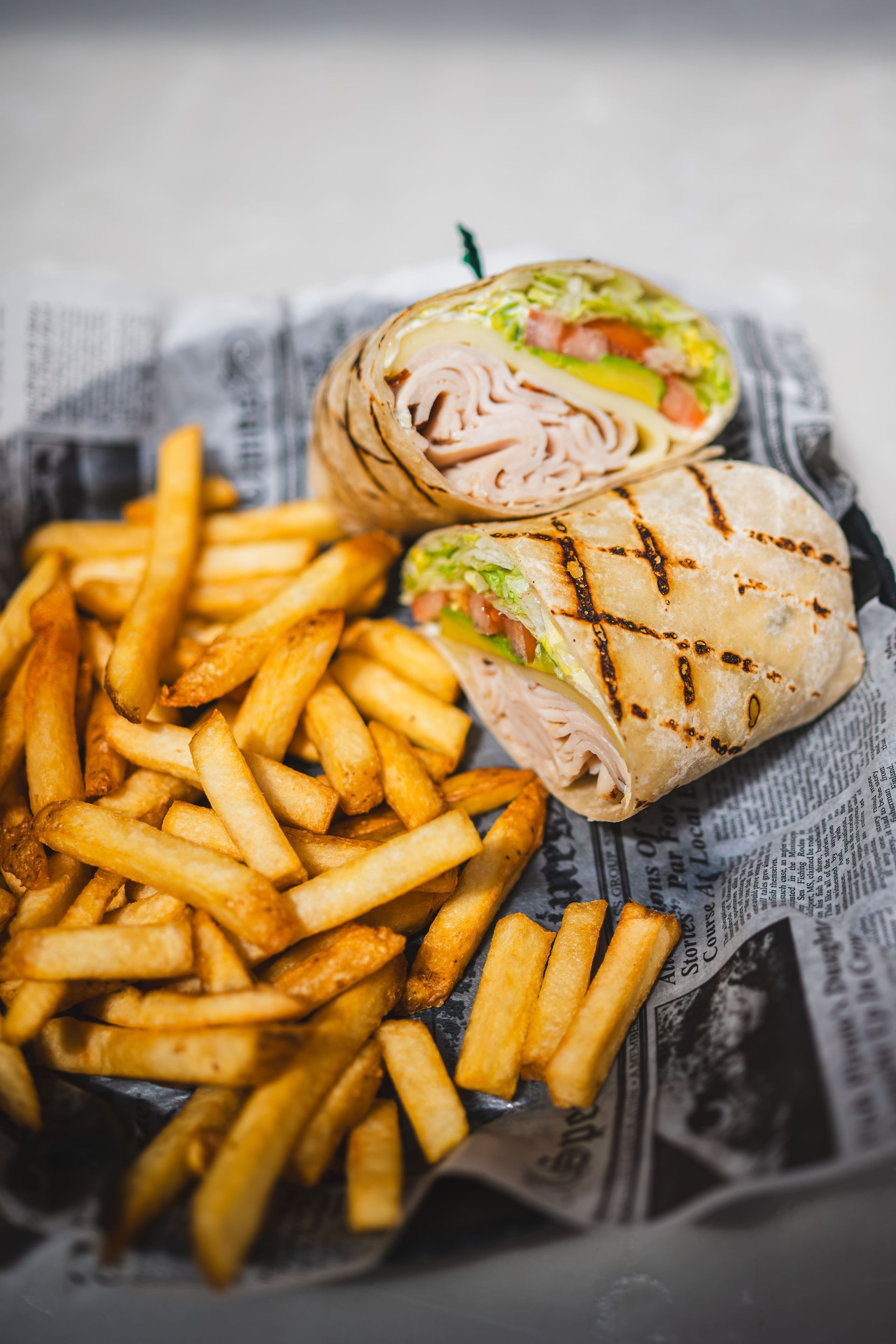 Grilled chicken wrap halves with lettuce and fries on newspaper-lined tray