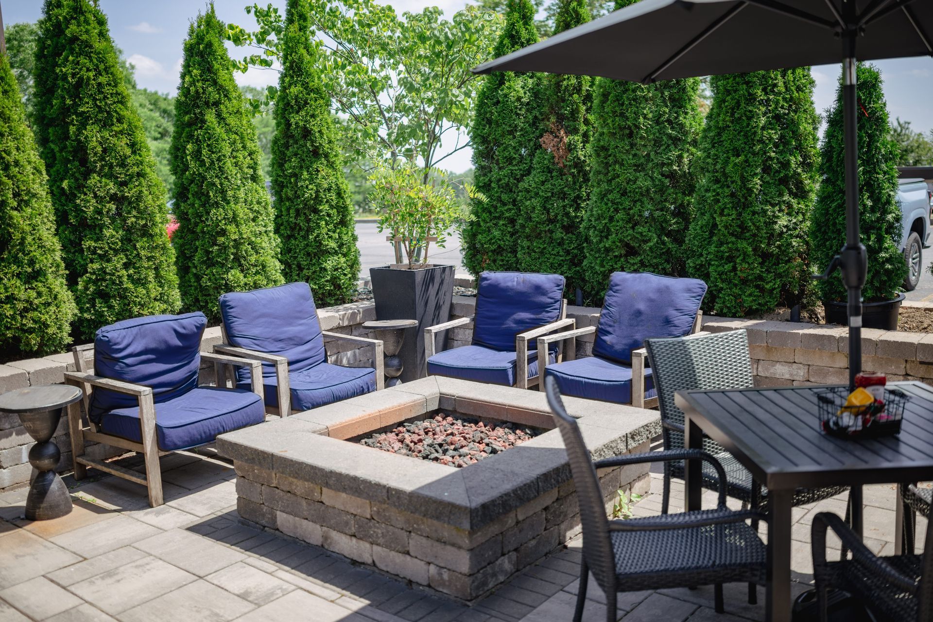 Patio with gray sectional seating, blue cushions, fire pit, and dining table under a black umbrella.