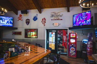 Sports bar interior with TVs, beer taps, neon signs, and a refrigerated drink display