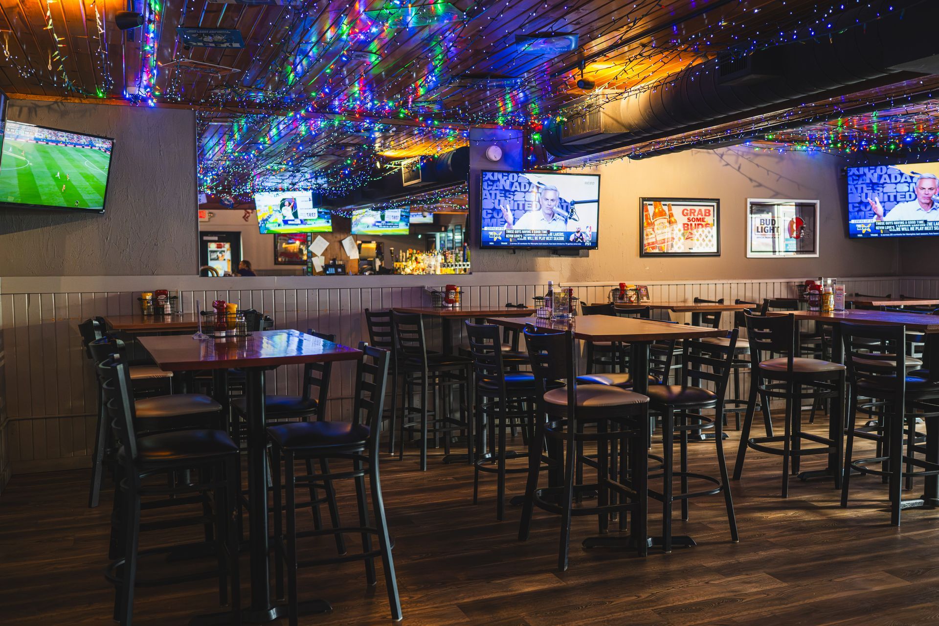 Empty sports bar with TVs, high tables, and colorful ceiling lights.